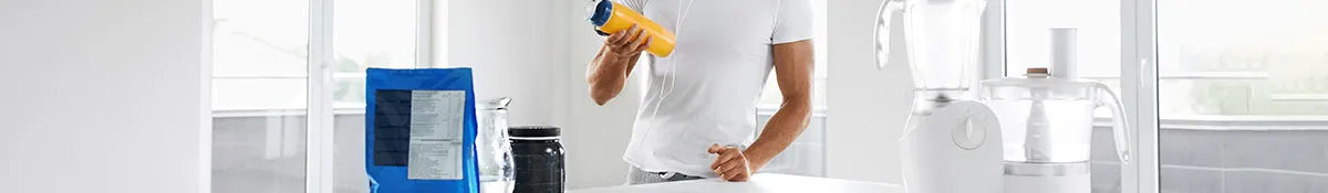 man holding protein shake bottle next to amino acid powders and blenders