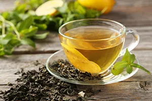 a cup of green tea surrounded by fresh green tea leaves