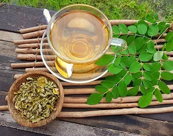 pot of dried moringa leaves next to a cup of green tea