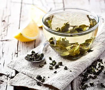 a glass filled with green tea leaves and hot water next to diced lemons