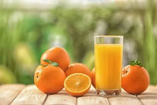 photograph of oranges next to a glass of orange juice