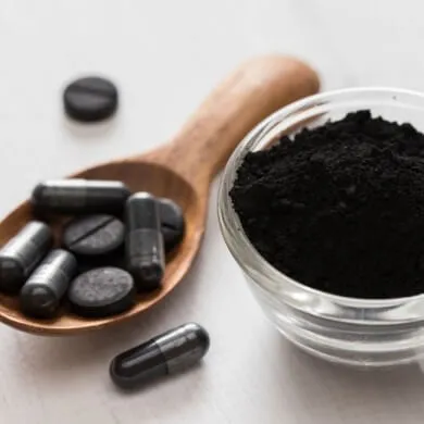 image of a spoon of activated charcoal powder with a cup of capsules next to it