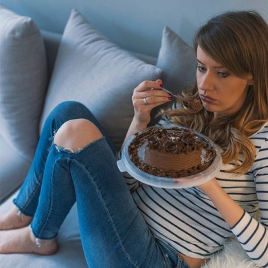 woman sitting on a sofa eating chocolate cake with moody face