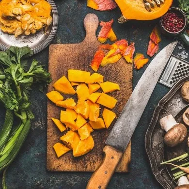 Diced pumpkin on a chopping board with a knife next to various vegetables