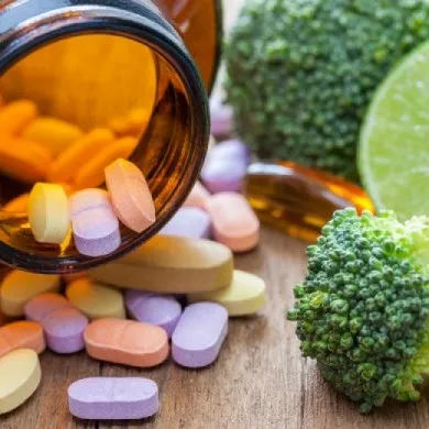 opened medicine bottle with tablets next to broccoli and a slice of lime