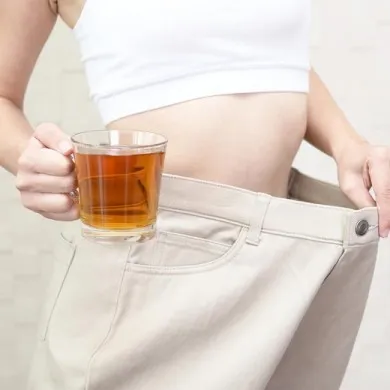 woman with oversized trousers showing space between trouser and waist holding a cup of slimming tea