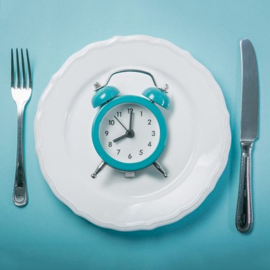 A dinner plate with knife and fork either side with a blue alarm clock in the middle of the plate
