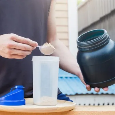 man putting protein powder fro a black tub using a spoon into protein shaker