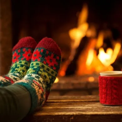 woman wearing christmas socks next to the fireplace with a cup of tea