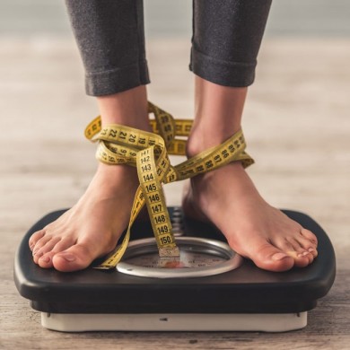woman standing on weighing scales that has a tape measure tied to her feet