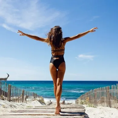 Woman walking towards a beach spreading her arms in the air
