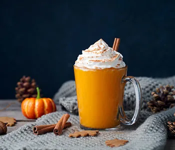 mug filled with pumpkin spiced latte and topped with whipped cream next to a small pumpkin