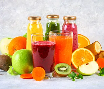Two different coloured smoothies in glasses in front of three bottled smoothies in front of different coloured fruits
