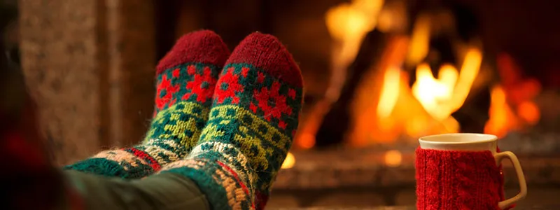 woman with christmas socks next to fire with a cup of tea