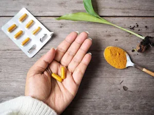 womans hand holding turmeric capsules nex to turmeric Powder